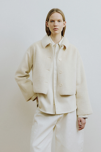 Person wearing a beige outfit standing against a plain white wall.