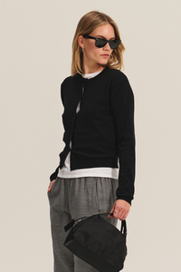 Person wearing a black sweater, gray pants, and black shoes holding a black bag on a white background