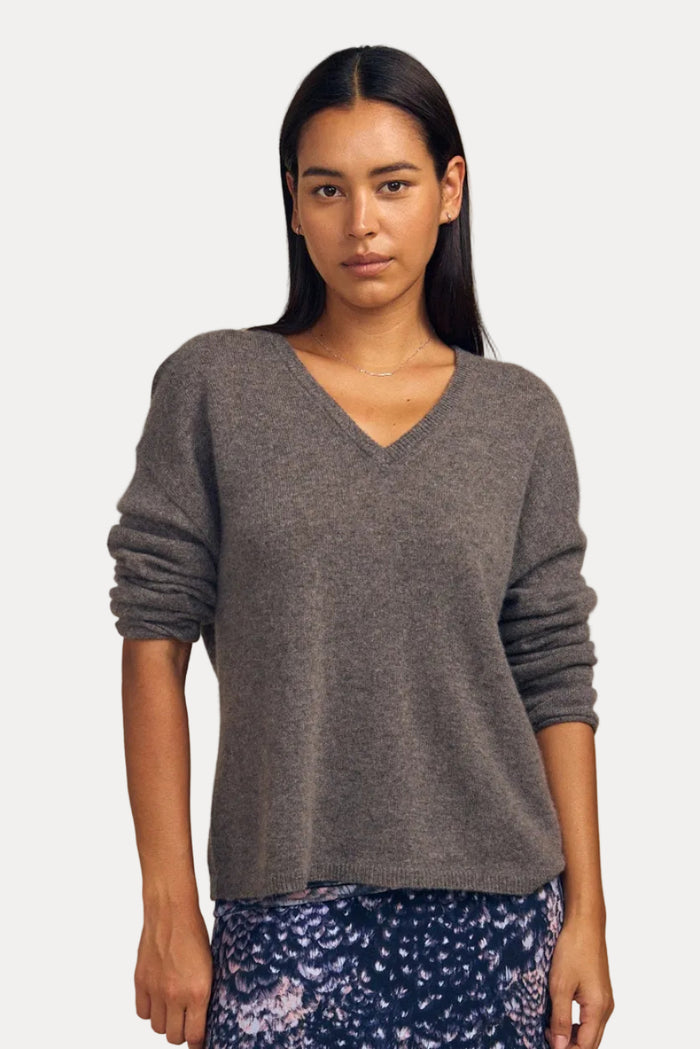 A woman modeling a heather gray long-sleeve V-neck sweater paired with a navy blue floral maxi skirt, set against a solid beige studio background.