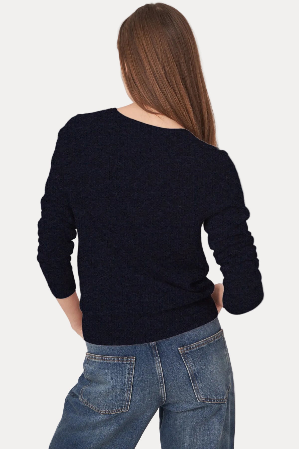 A woman shown from the back wearing a dark navy knit sweater and blue jeans against a plain light background.