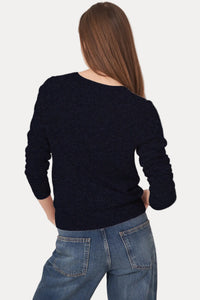 A woman shown from the back wearing a dark navy knit sweater and blue jeans against a plain light background.
