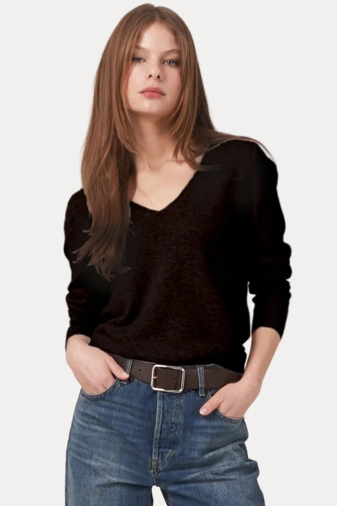 A woman modeling a black long-sleeve knit top, blue high-waisted straight-leg jeans with rolled cuffs, a dark belt, and dark brown boots, against a plain light gray studio background.