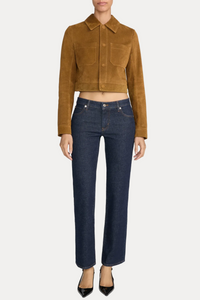 A model wearing a cropped tan suede jacket and dark blue straight-leg jeans, standing against a light gray studio background.