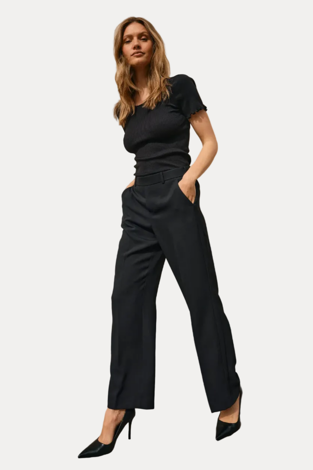 Woman wearing a black outfit standing against a beige wall.