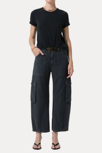 A model wearing a black short-sleeve t-shirt and dark charcoal gray wide-leg cargo pants with a black belt, styled with black sandals and a gold necklace against a light gray studio background.