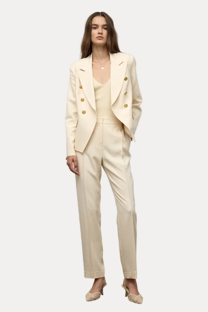 Woman wearing a beige suit standing against a plain background