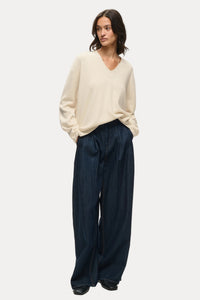 A woman modeling a cream V-neck knit sweater and dark navy wide-leg trousers against a plain white studio background.