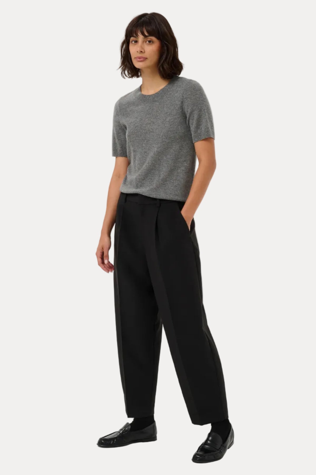 A woman modeling a short-sleeve gray knit top and black wide-leg trousers against a plain light gray studio background.