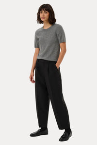 A woman modeling a short-sleeve gray knit top and black wide-leg trousers against a plain light gray studio background.
