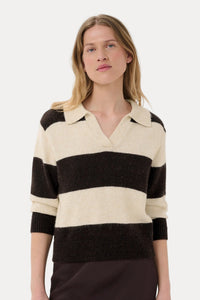A woman wearing a knit polo-style sweater with wide horizontal stripes in cream and dark brown, paired with a dark brown skirt, against a plain light gray studio background.