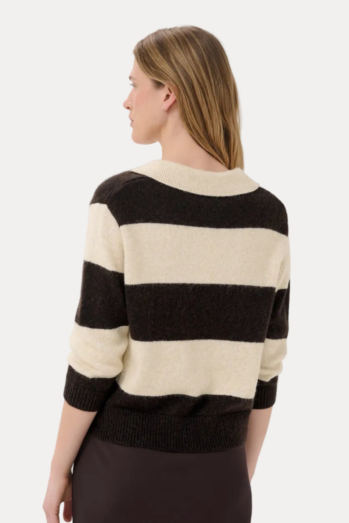 A woman shown from the back wearing a fuzzy knit sweater with wide horizontal black and cream stripes, paired with a dark skirt, against a light gray studio background.