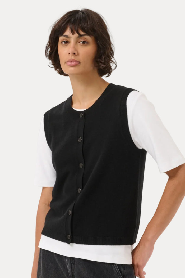 A model wearing a black sleeveless button-front knit vest over a white short-sleeve t-shirt and dark gray jeans, photographed against a light gray studio background.