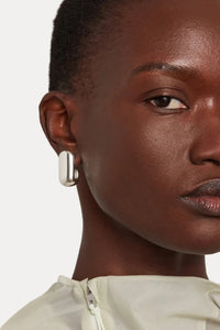 Close-up of a model wearing a single silver-toned geometric stud earring with a polished rectangular bar design.