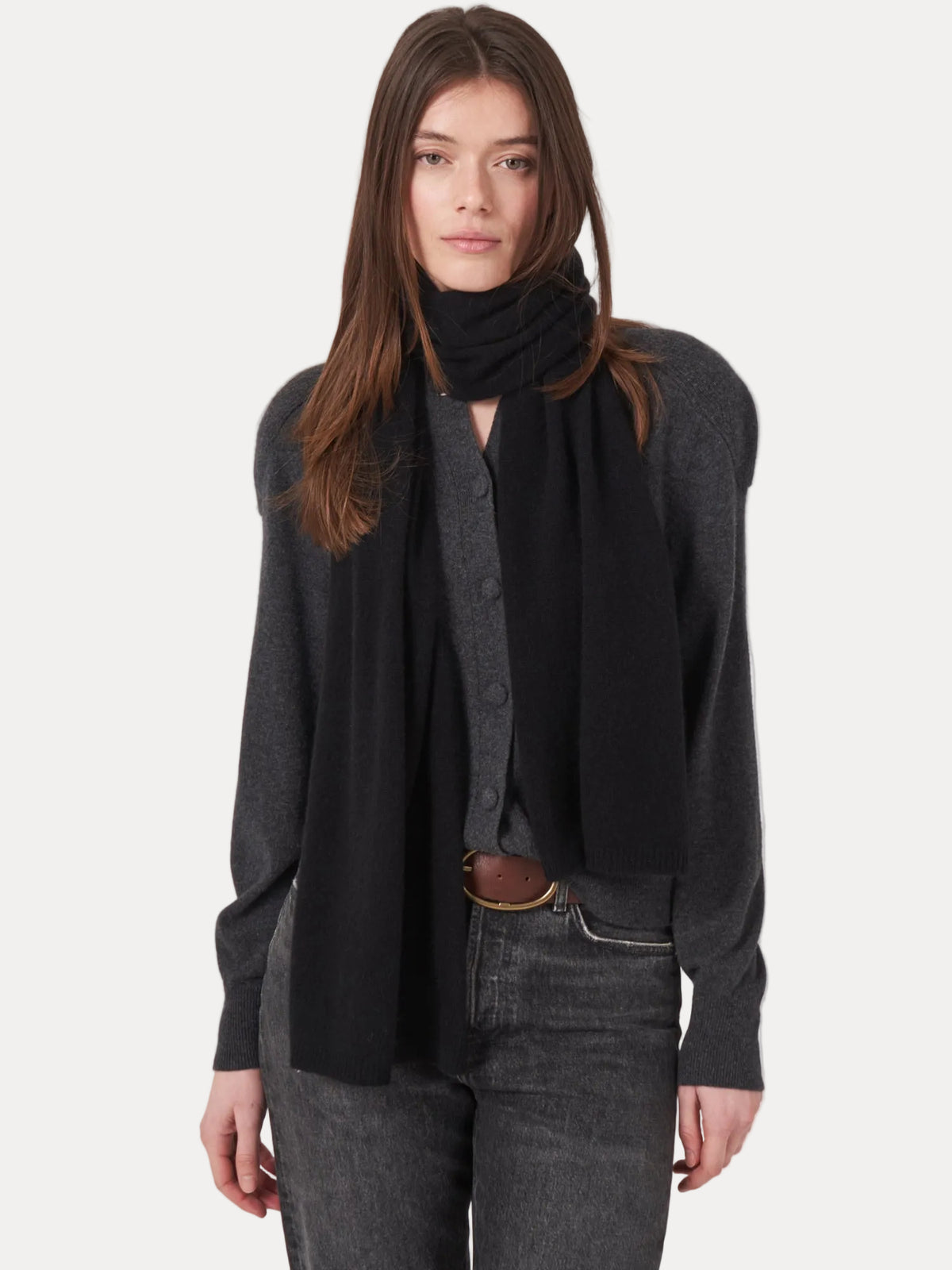 Woman wearing a dark gray cardigan, black scarf, and jeans on a white background