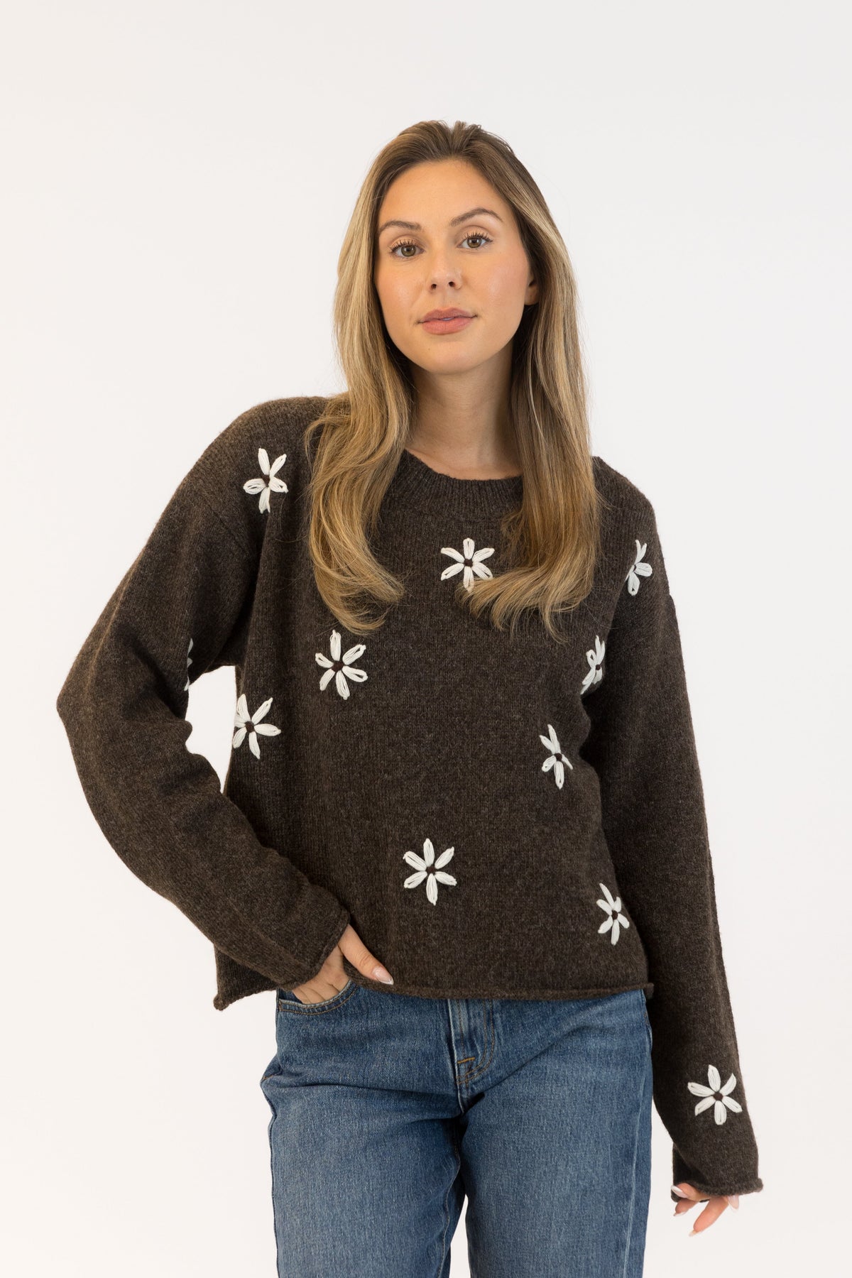 Woman wearing a brown sweater with white floral patterns on a white background