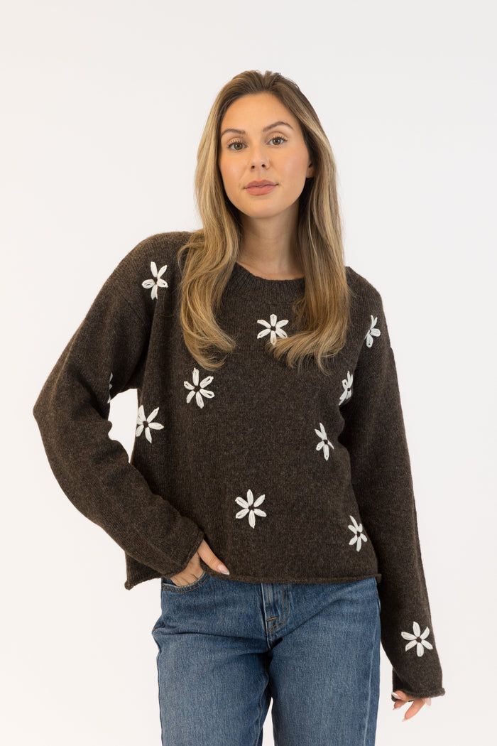 Woman wearing a brown sweater with white floral patterns on a white background