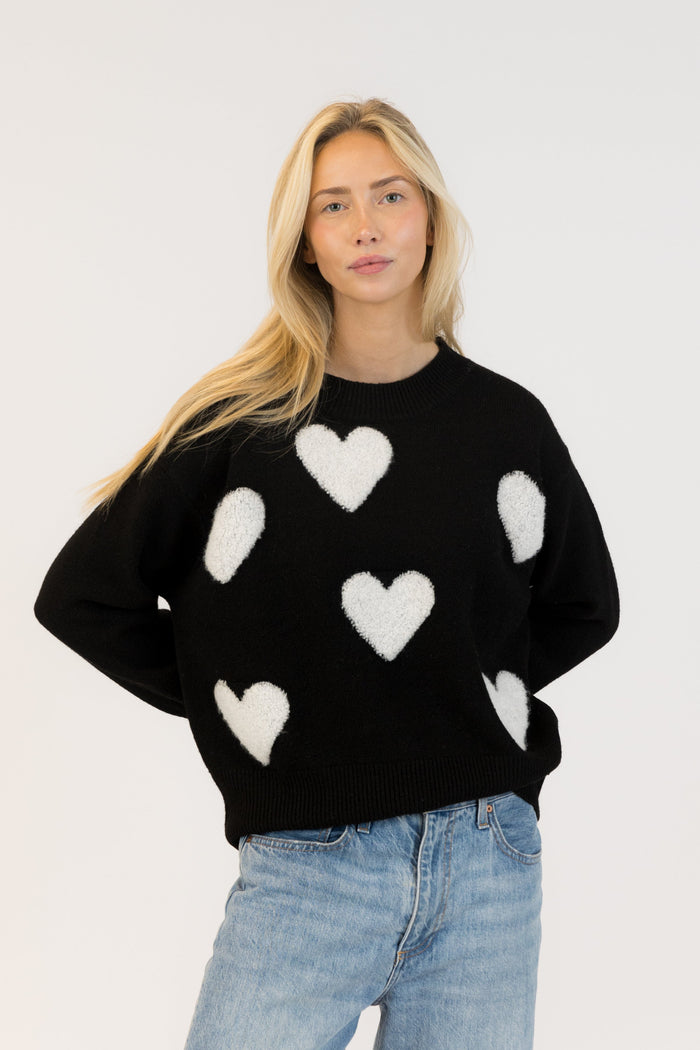 Woman wearing a black sweater with white heart patterns on a plain background