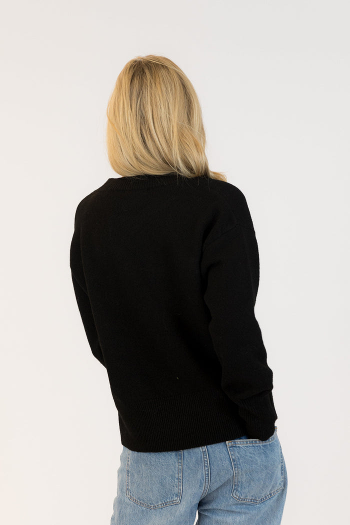 Person wearing a black sweater and blue jeans on a white background