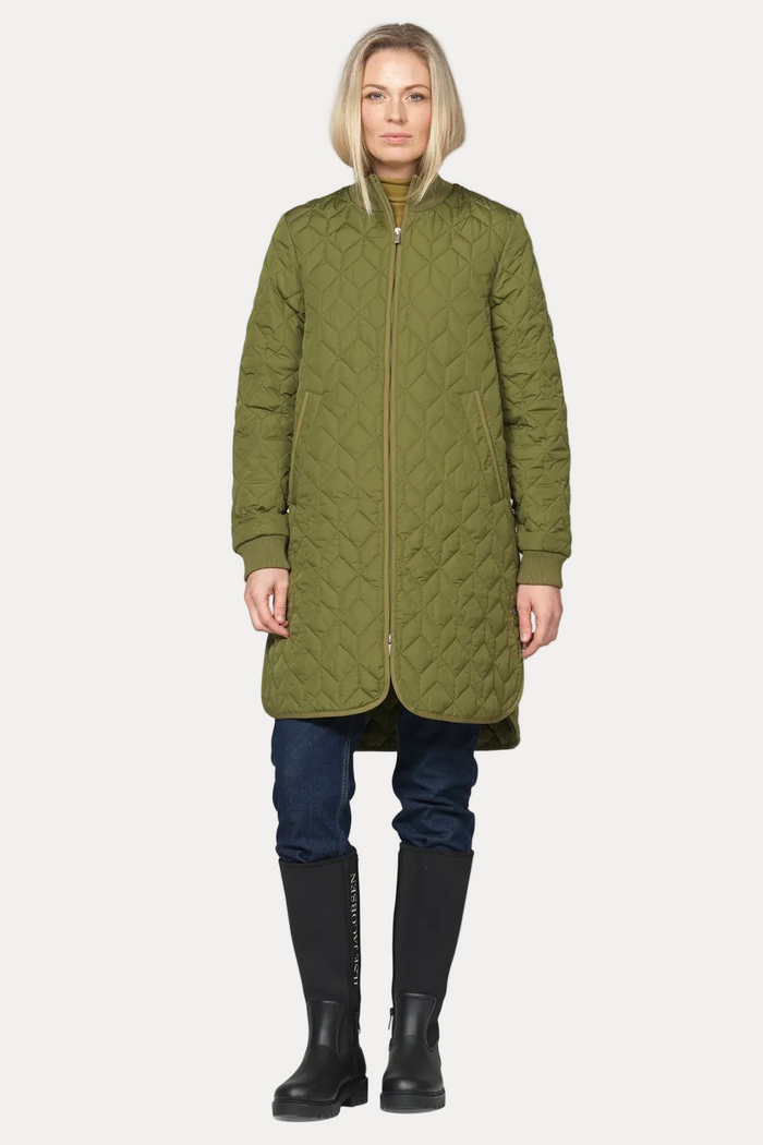 A woman modeling a long olive green quilted coat with a full front zipper, paired with dark blue jeans and black rain boots, against a plain off-white background.