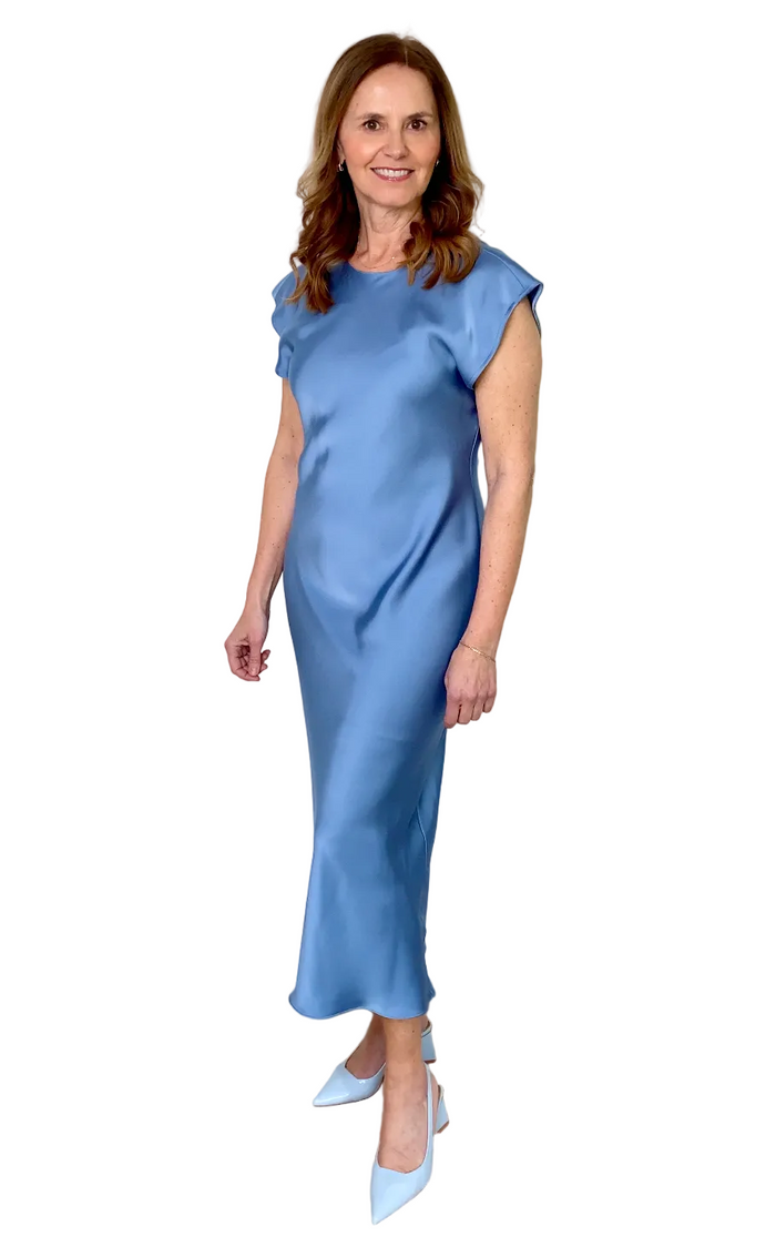 Woman wearing a blue dress standing against a white wall.