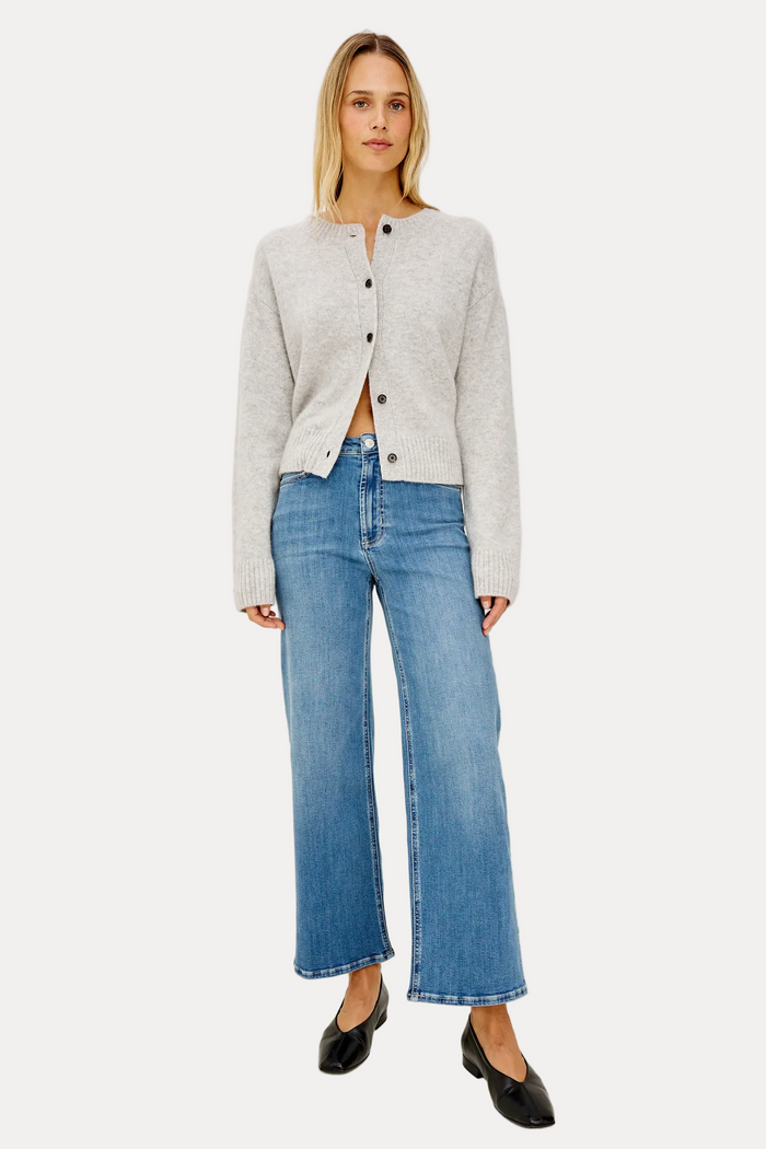A woman modeling a light gray cropped button-front cardigan with wide sleeves, paired with blue wide-leg jeans and black pointed flats, against a plain white studio background.