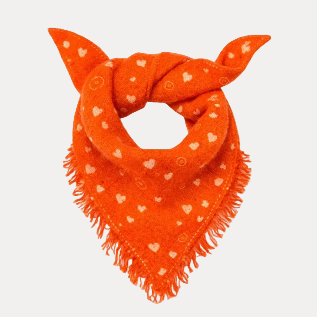 An orange knit bandana or scarf with white heart and swirl patterns and fringed edges, styled as a loop on a solid white background.