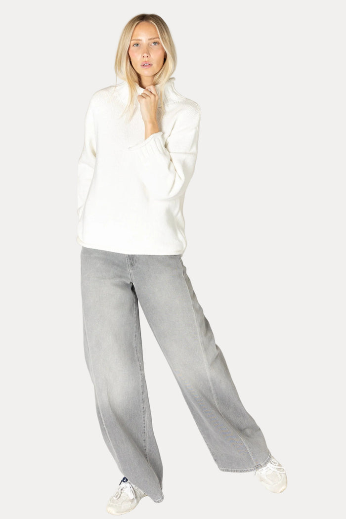 Woman wearing a white blouse and gray pants on a plain background