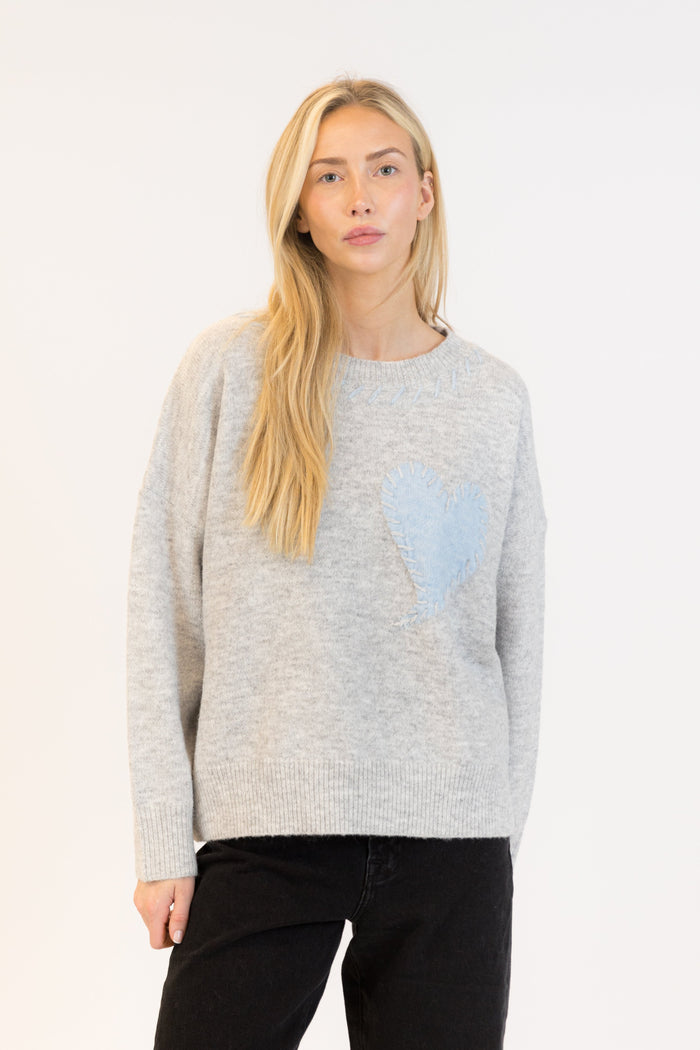 Woman wearing a light gray sweater with a blue heart design on a white background