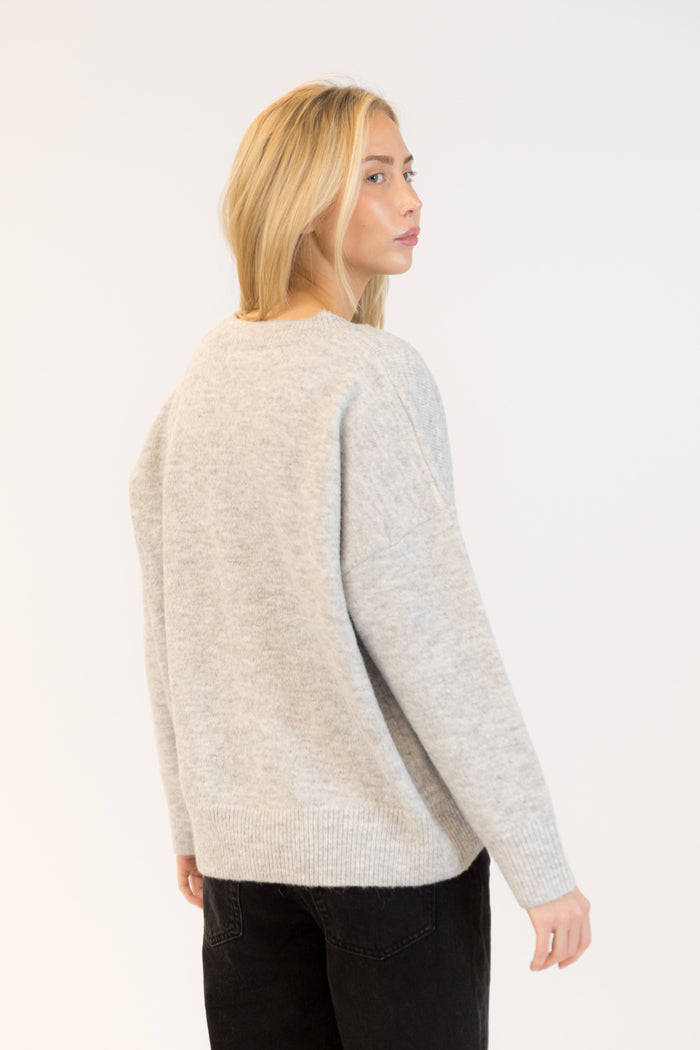 Woman wearing a light gray sweater with black pants on a white background