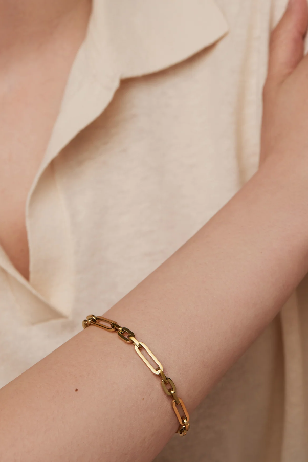 Gold chain bracelet on a person wearing a beige shirt.