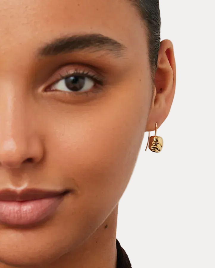 Close-up of a woman wearing gold hoop earrings with a neutral background