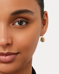 Close-up of a woman wearing gold hoop earrings with a neutral background