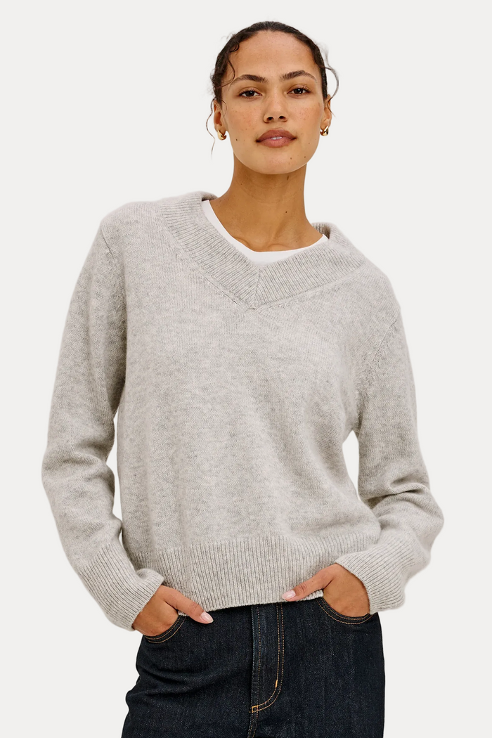 Woman wearing a gray sweater and dark jeans against a plain background