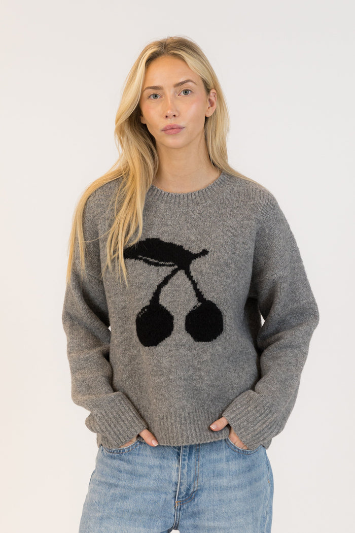 Woman wearing a gray sweater with black cherry design on a plain background