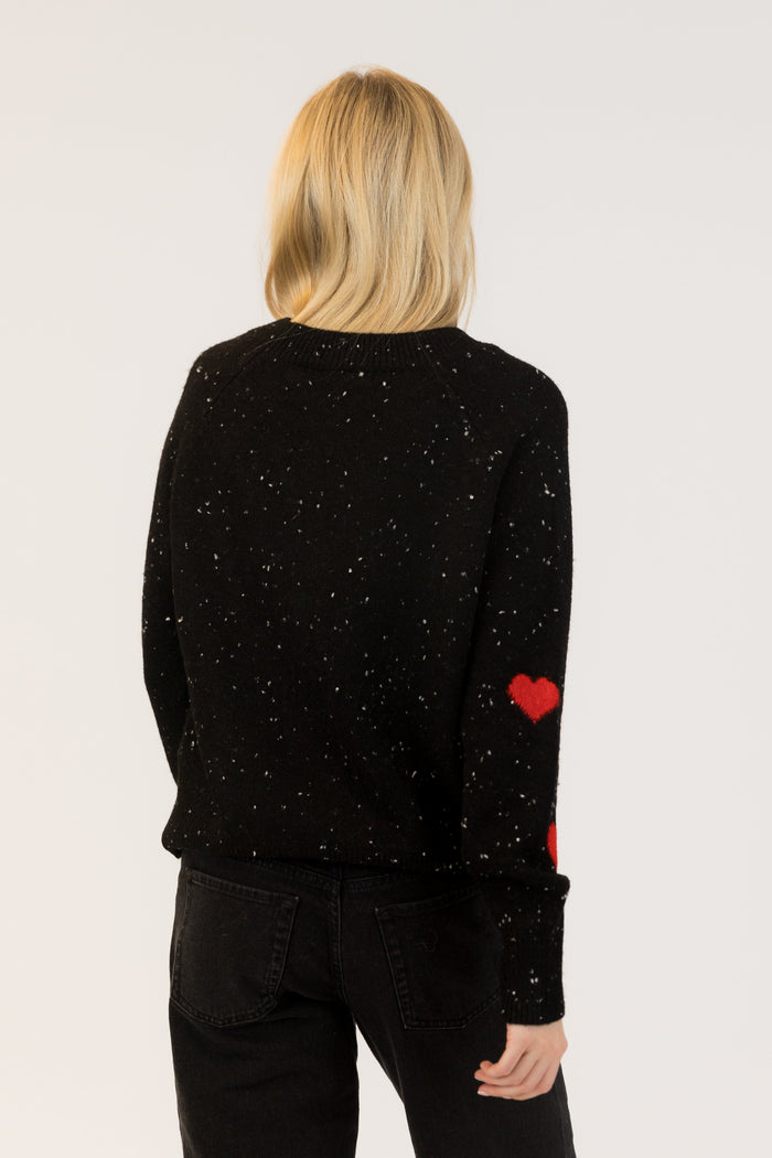 Person wearing a black sweater with red heart design on sleeves against a white background
