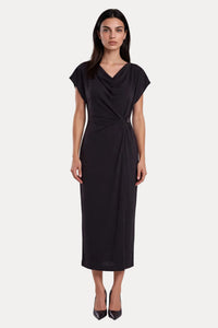 A woman modeling a black midi dress with a draped neckline, short cap sleeves, and a twisted waist detail, photographed against a light gray studio background.