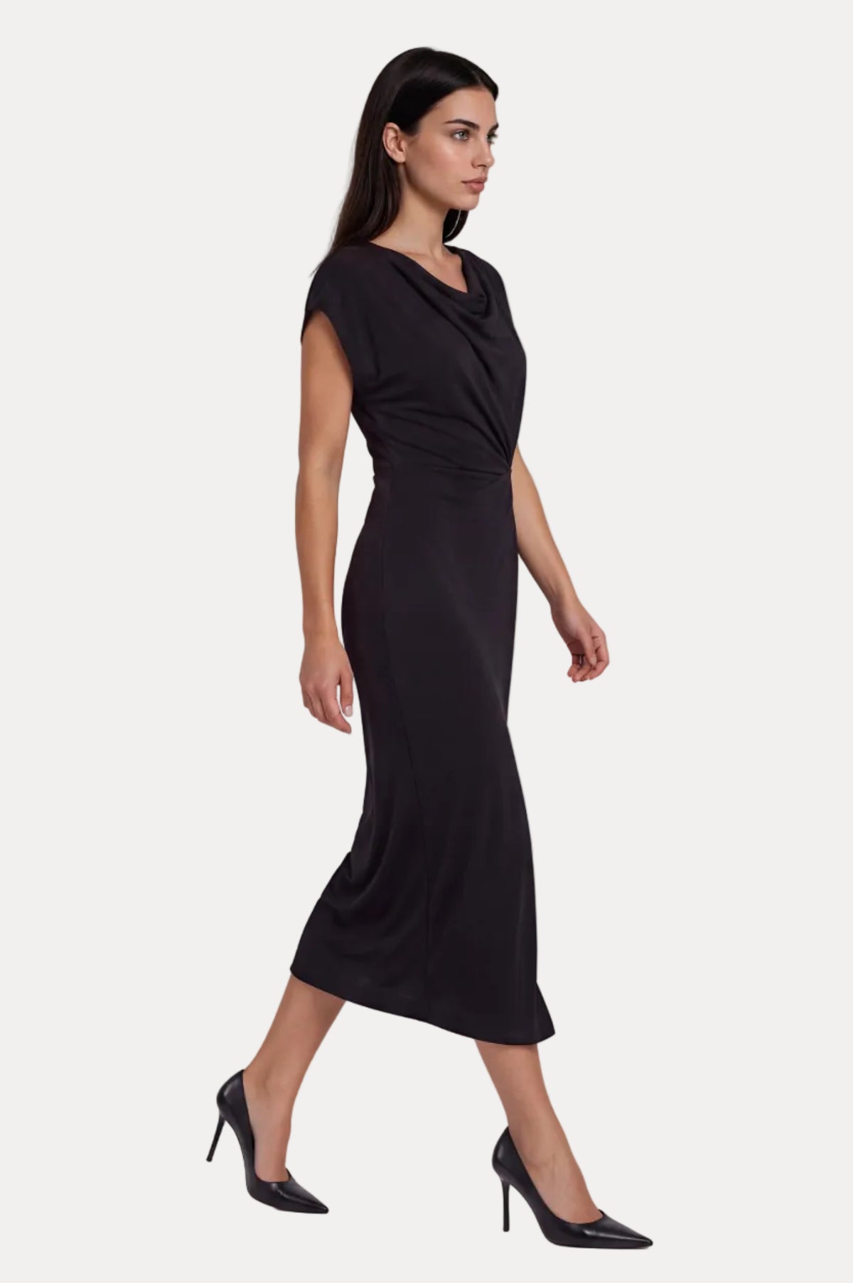 A woman modeling a black midi dress with a draped cowl neckline and cap sleeves, paired with black pointed-toe heels, against a light gray studio background.