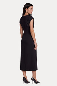 A woman modeling a black sleeveless midi dress from the back, paired with black pointed-toe heels, against a light gray studio background.