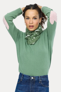 Woman wearing a green sweater with pink sleeves and blue jeans on a white background