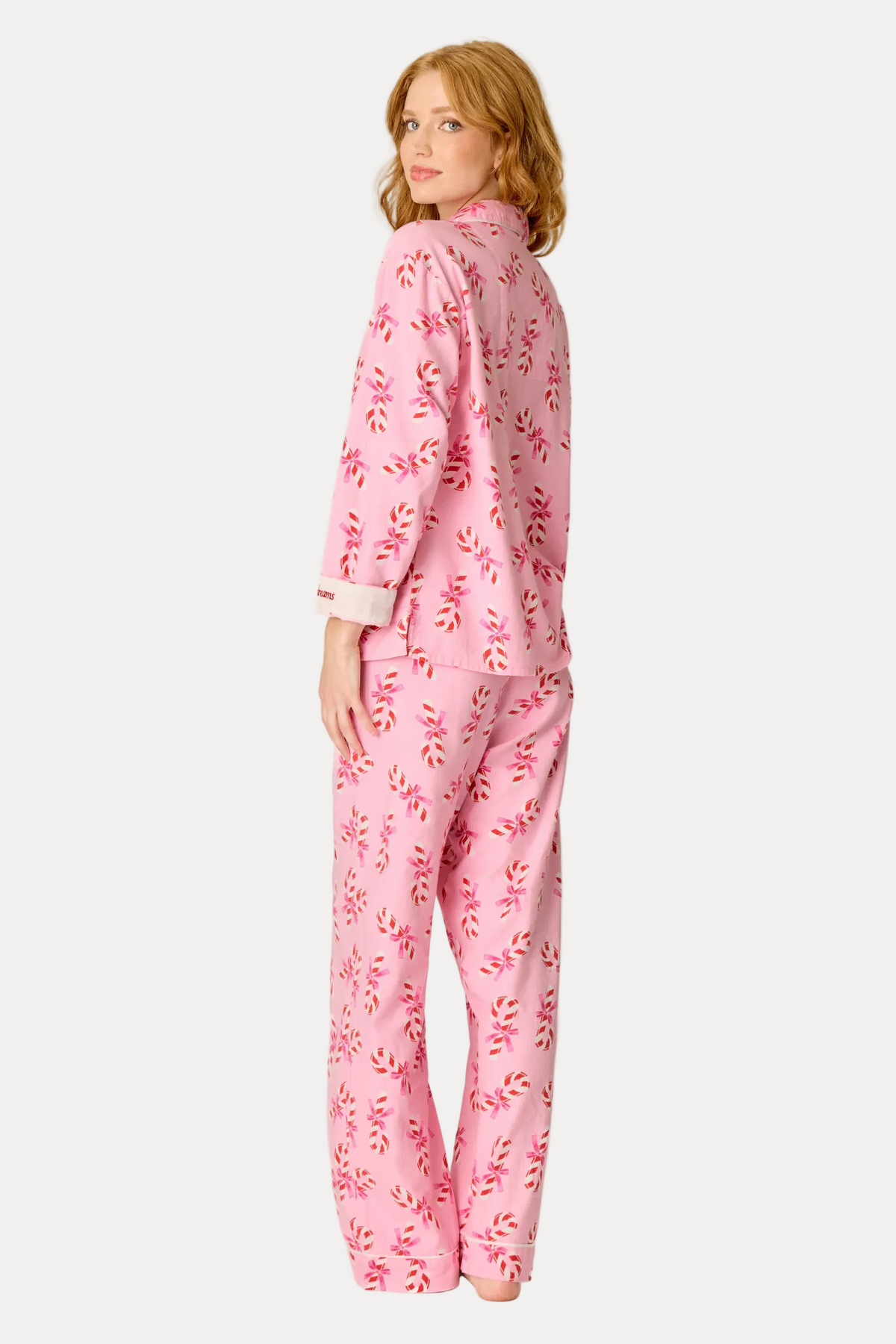 A woman modeling a pink pajama set with a red and white leaf pattern, shown from the back against a plain white studio background.