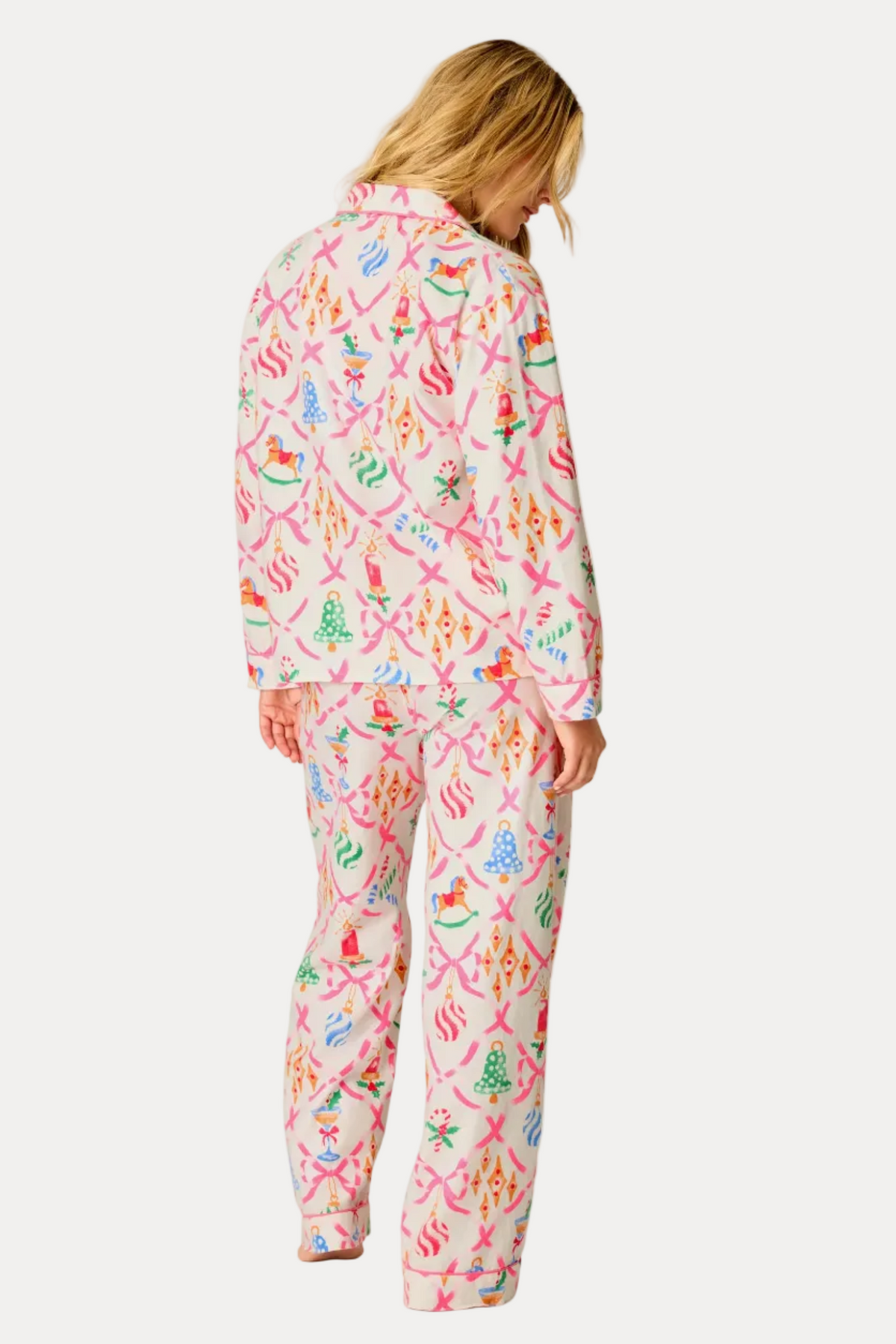 A woman wearing a matching pink pajama set with a colorful beach-themed print, shown from the back against a plain off-white studio background.