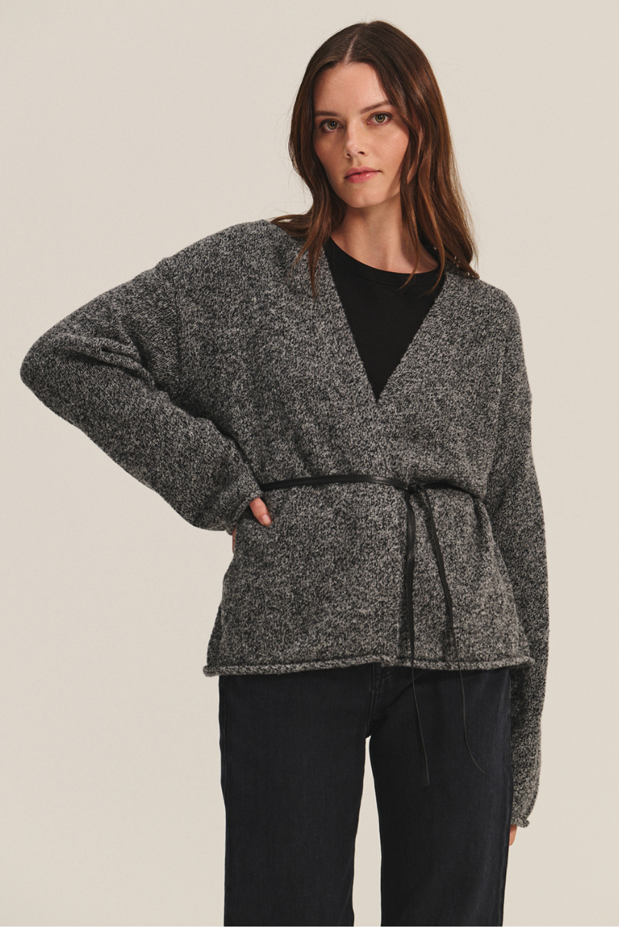 Woman wearing a gray knitted cardigan over a black top and pants on a beige background
