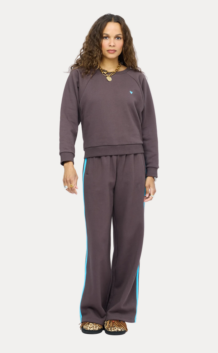 A woman modeling a matching dark brown sweatshirt and wide-leg sweatpants set with bright blue side stripes, photographed against a light gray studio background.