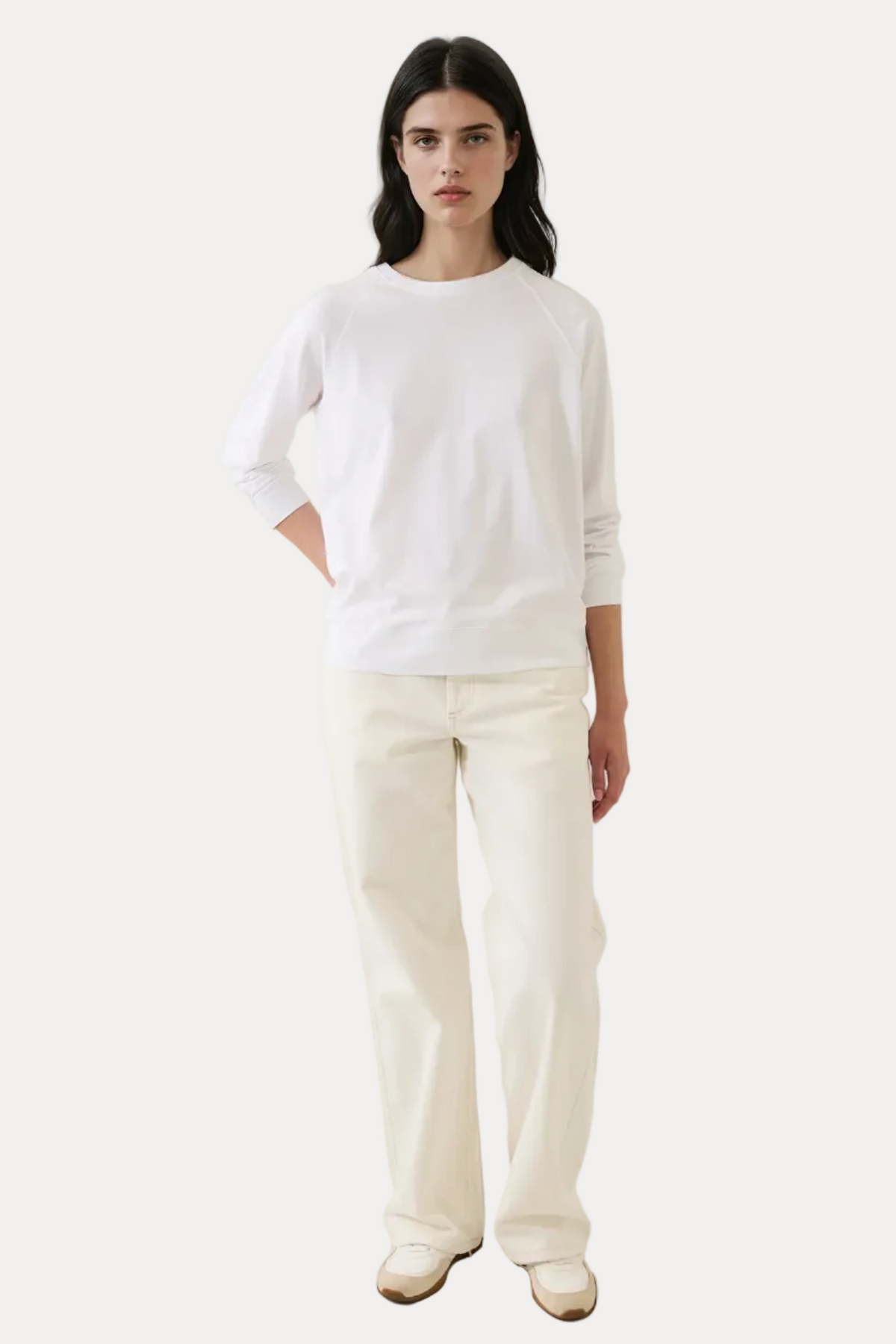 Person wearing a white top and cream pants against a plain background