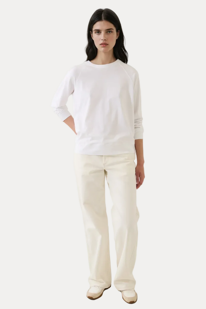 Person wearing a white top and cream pants against a plain background