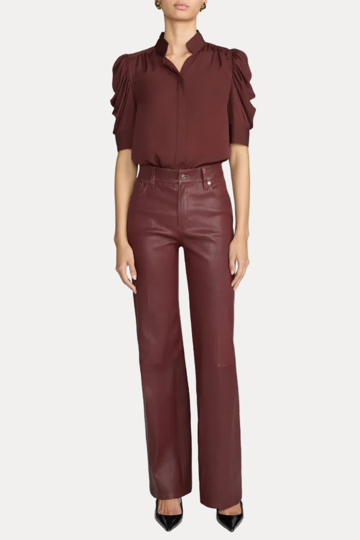 A model wearing a dark burgundy blouse with dramatic ruffled short sleeves and matching high-waisted burgundy wide-leg pants, paired with black pointed-toe heels, against a light gray studio background.