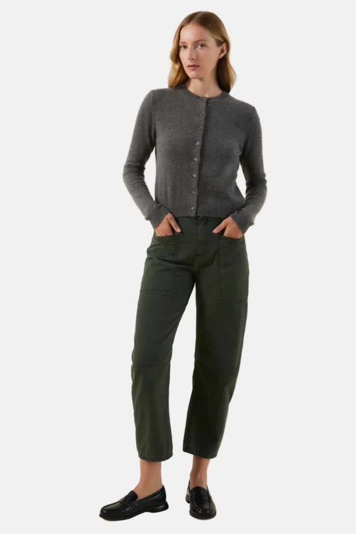 A woman modeling a dark gray button-up cardigan sweater, dark green cropped trousers, and black loafers against a solid light beige studio background.