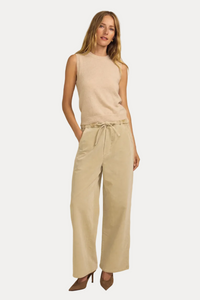 A woman modeling a sleeveless light beige knit top and matching wide-leg trousers with a drawstring waist, paired with brown pointed-toe heels, against a solid warm beige studio background.