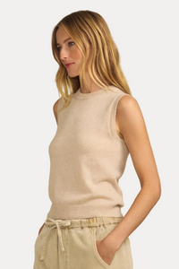 A woman wearing a sleeveless knit sweater vest in a light beige color, paired with matching beige drawstring pants, set against a solid beige background.