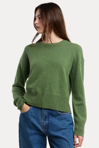 Person wearing a green sweater and blue jeans on a beige background